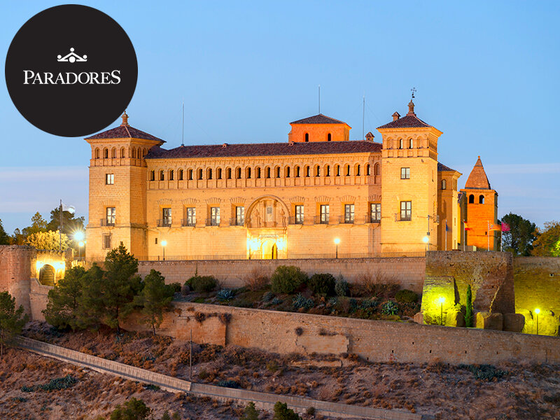 Fortaleza histórica española iluminada en una colina al atardecer.