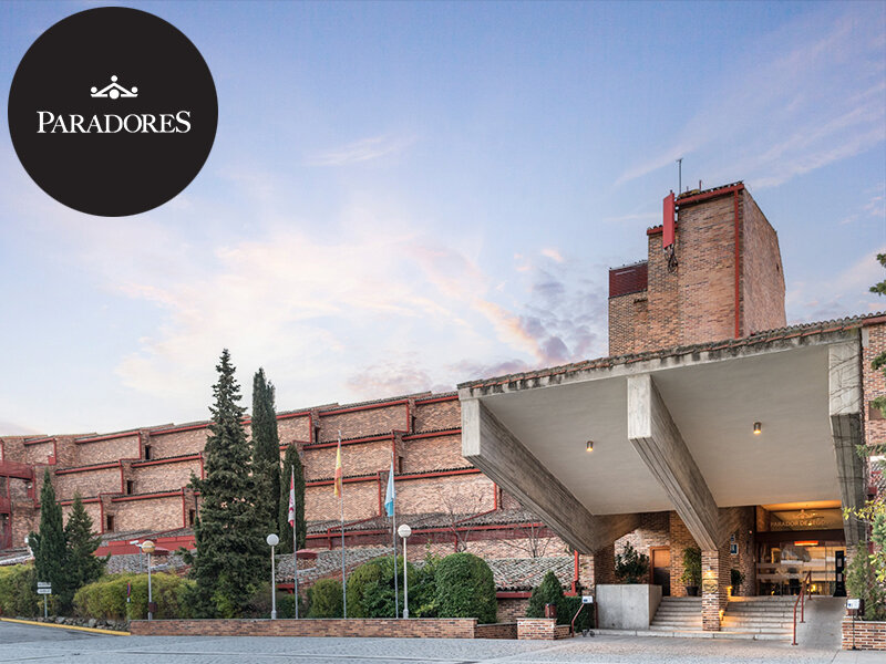 Edificio moderno de ladrillo con gran marquesina de entrada de hormigón y árboles al atardecer.