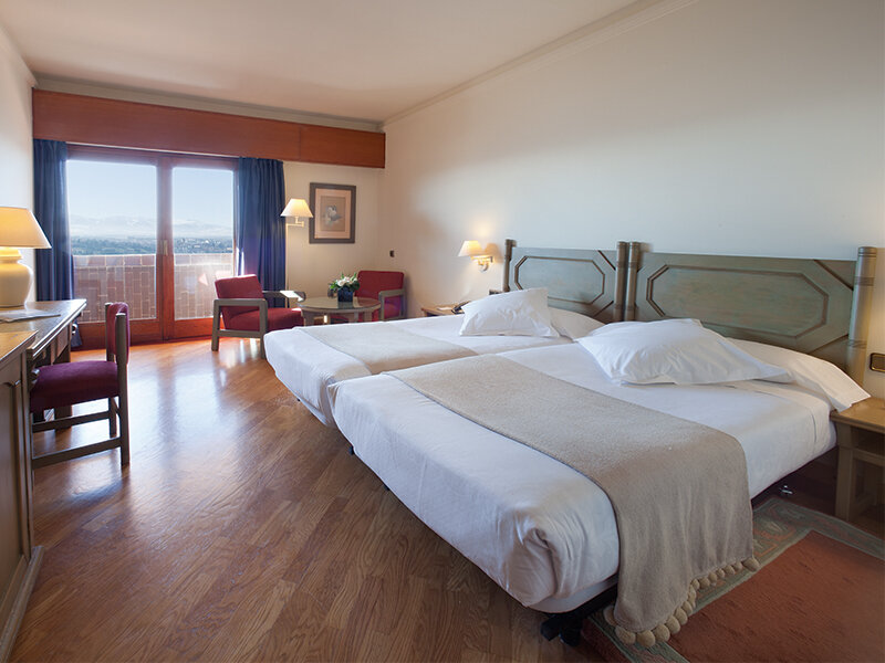 Una habitación de hotel espaciosa con dos camas, suelo de madera, escritorio y un gran ventanal.