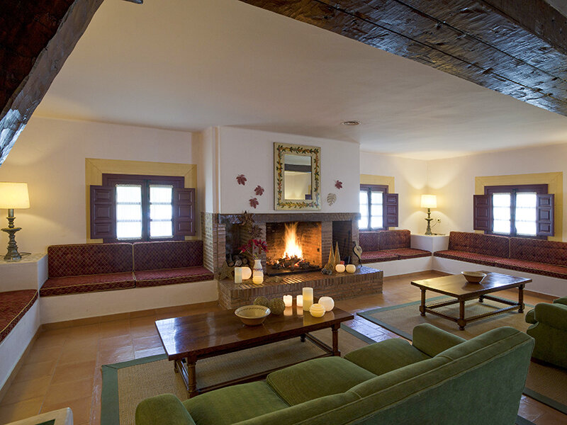 Acogedora sala con chimenea, paredes blancas, vigas de madera, asientos rojos y sofás verdes.