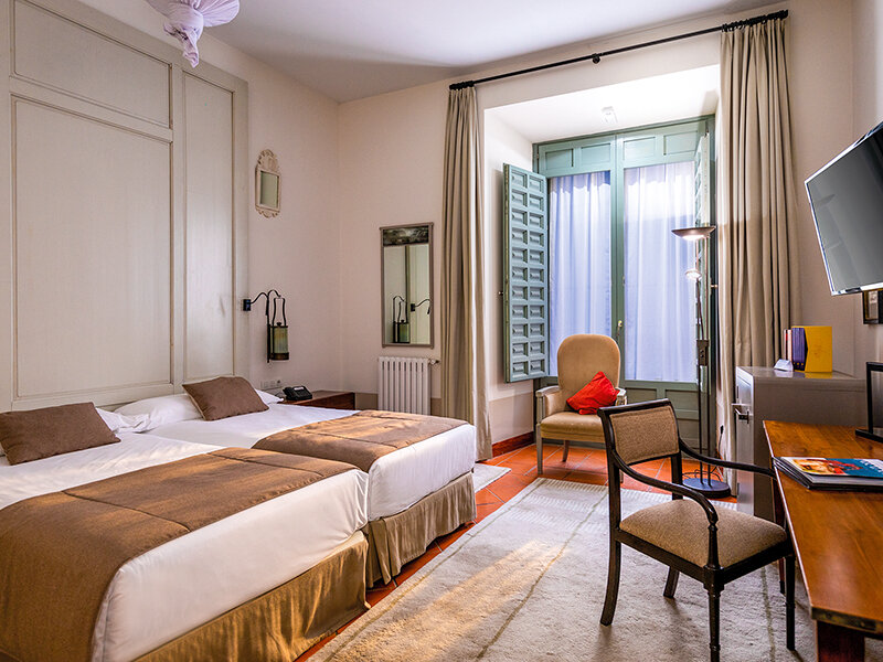 Una acogedora habitación de hotel con dos camas, un escritorio, un sillón y una ventana con cortinas.