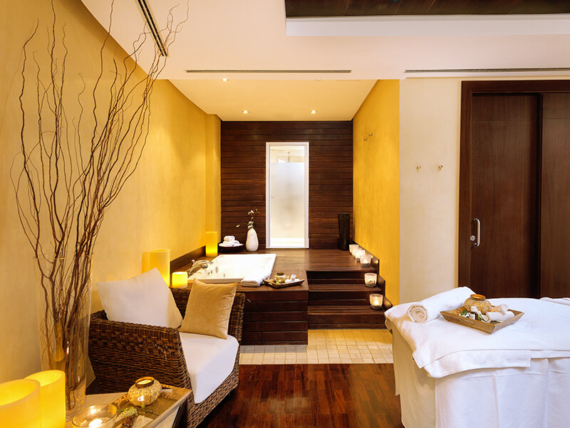 Lujosa sala de spa con jacuzzi, paredes de madera, camilla de masajes, paredes amarillas y velas.