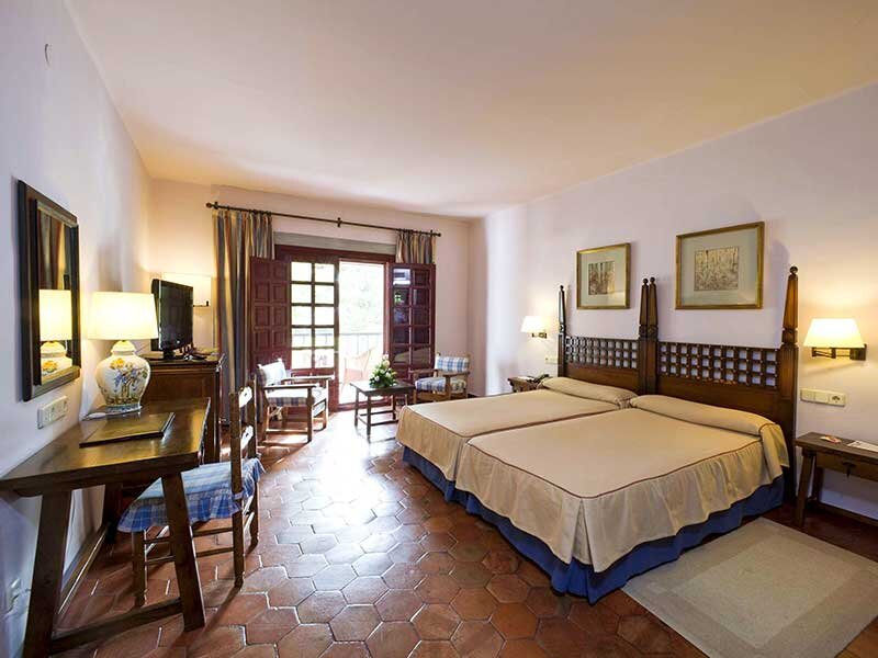 Una acogedora habitación de hotel con dos camas, muebles de madera, suelo de baldosas y balcón abierto.