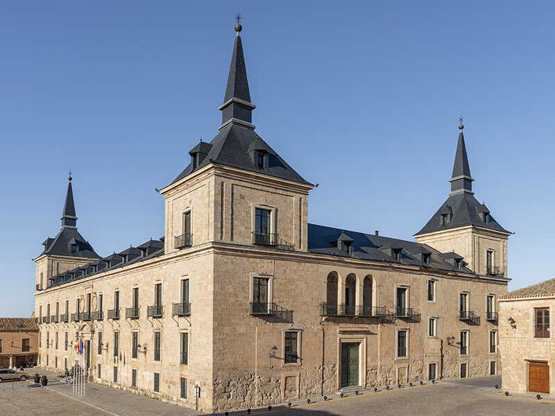 Un gran edificio renacentista marrón claro con tres torres puntiagudas de pizarra y cielo azul de fondo.