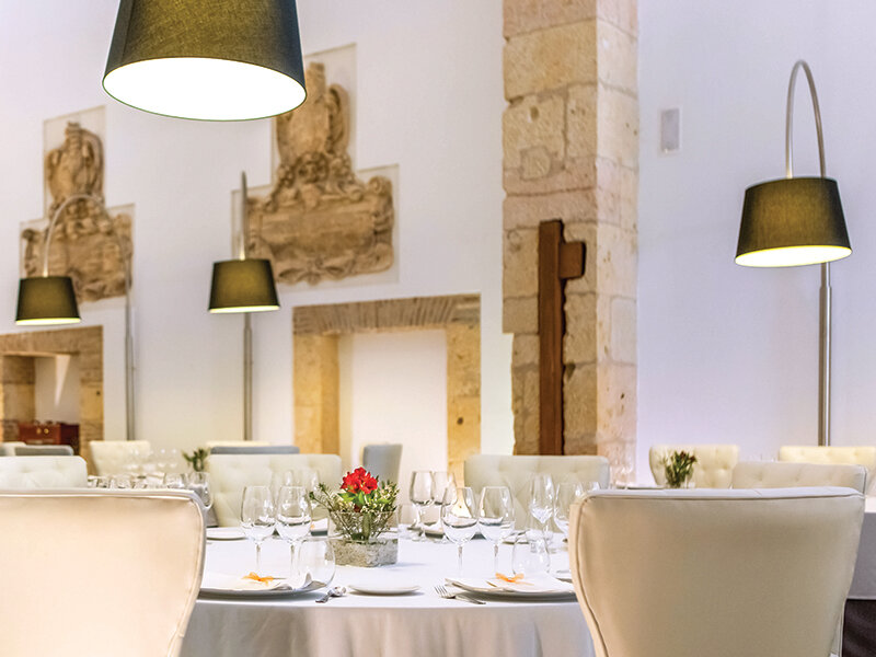 Elegante restaurante con mesas blancas, sillones de cuero y luz cálida de lámparas modernas.