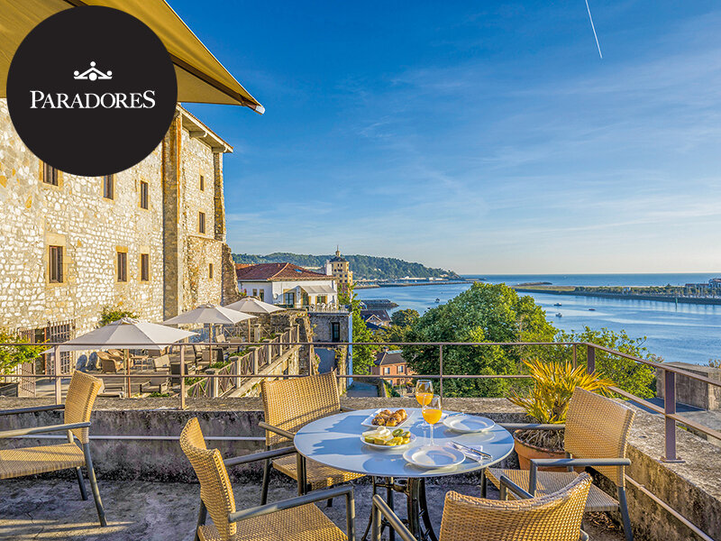 Una terraza soleada con mesa de comedor con vistas a una bahía pintoresca y edificios de piedra.