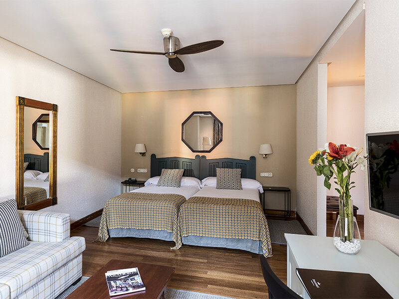 Una acogedora habitación de hotel con dos camas, un sofá, suelos de madera y un ventilador de techo.