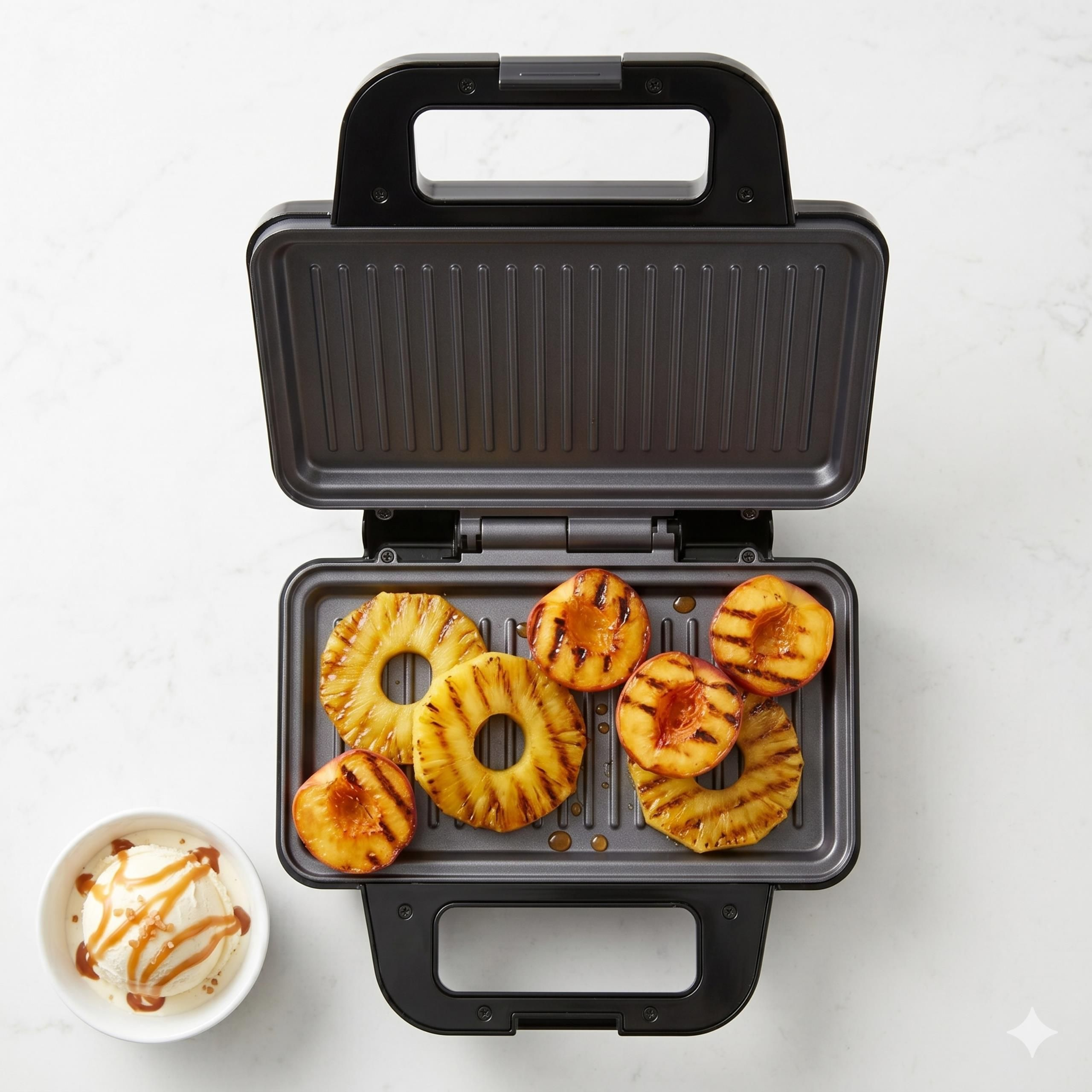 Grillowany ananas i brzoskwinie w otwartym czarnym grillu, obok miseczka lodów z sosem karmelowym.