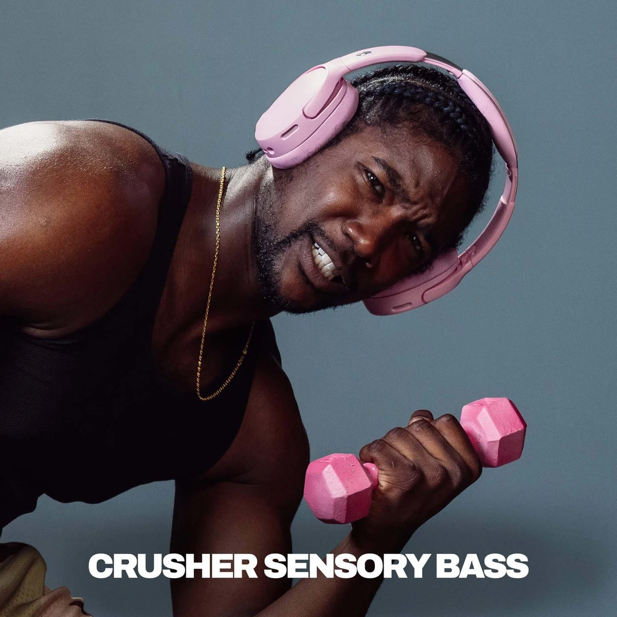 Un hombre con auriculares rosas levanta una mancuerna rosa sobre fondo gris.