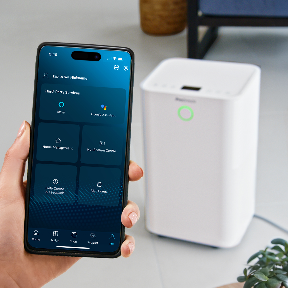 Hand hält Smartphone mit Smarthome-App, daneben ein weißer Luftentfeuchter.