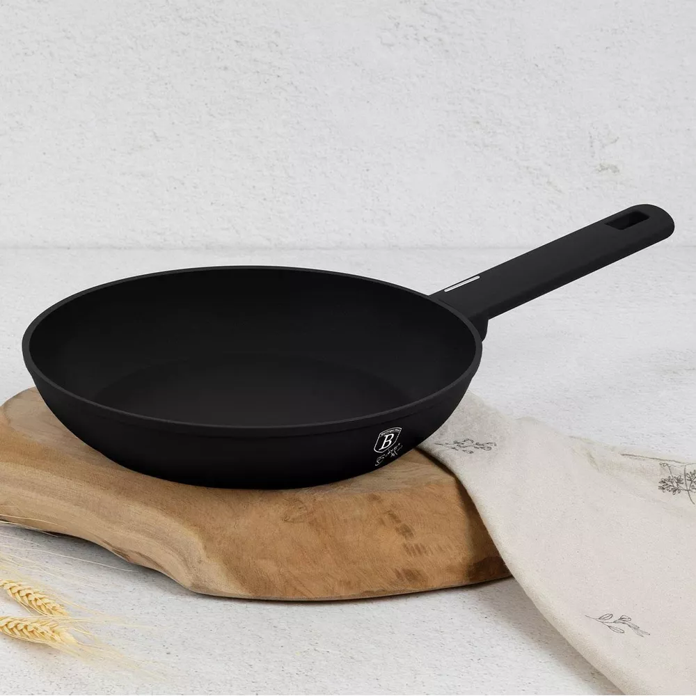 Une poêle noire repose sur une planche en bois avec un torchon blanc et des épis de blé.