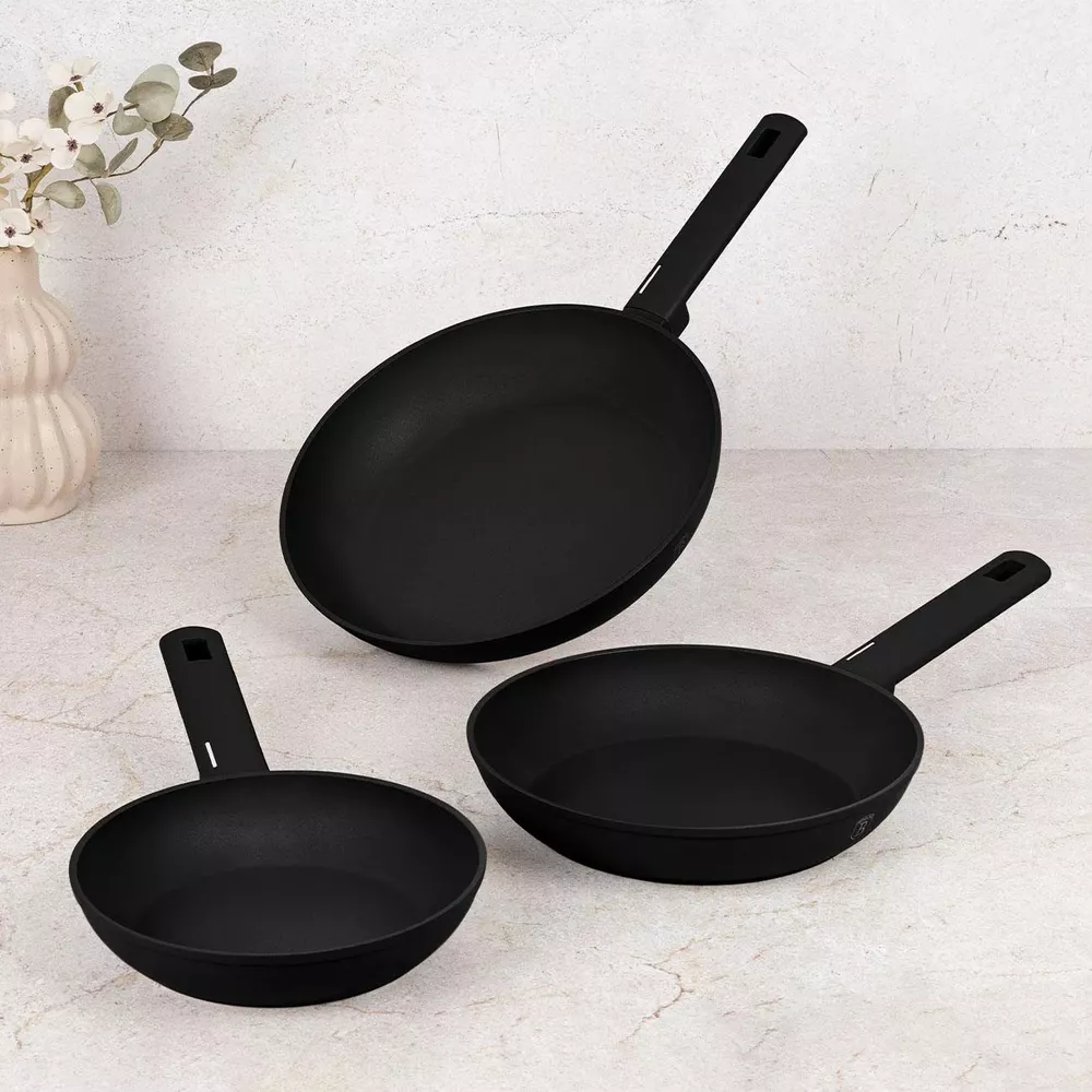 Trois poêles à frire noires de différentes tailles reposent sur un comptoir en marbre.