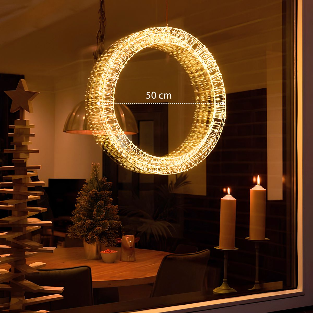 Een verlichte ring van 50 cm hangt voor een raam, met een houten kerstboom en kaarsen in een gezellige kamer.