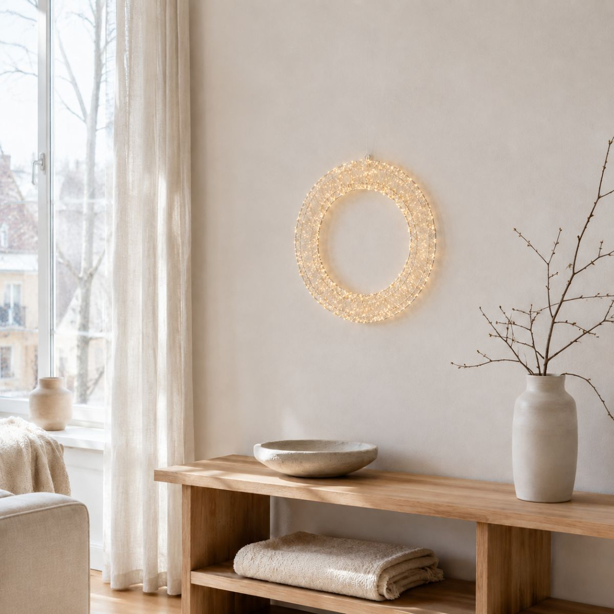 Verlichte krans op beige muur boven houten tafel met vaas, schaal en opgevouwen doek.