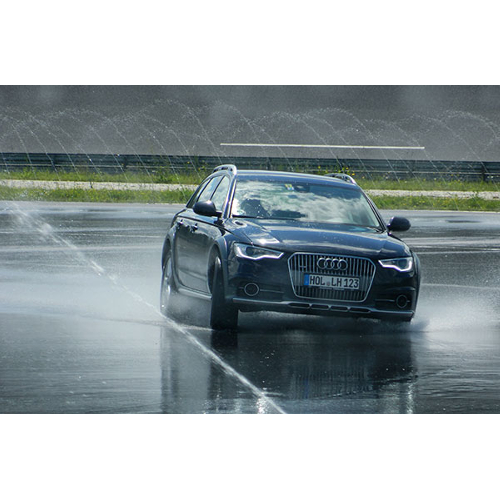 Ein schwarzes Audi-Auto fährt auf nasser Strecke mit Wassersprühnebel im Hintergrund.