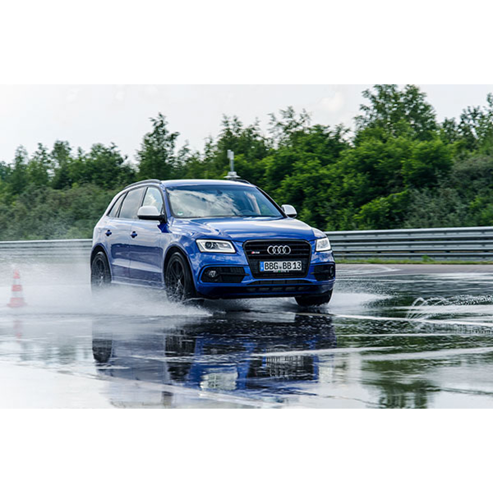 Ein blauer Audi fährt auf einer nassen Teststrecke und wirft Spritzwasser auf.