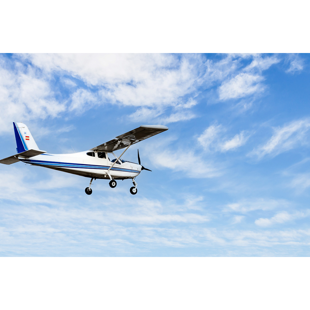 Ein kleines weißes Propellerflugzeug mit blauen Streifen fliegt am blauen Himmel mit weißen Wolken.