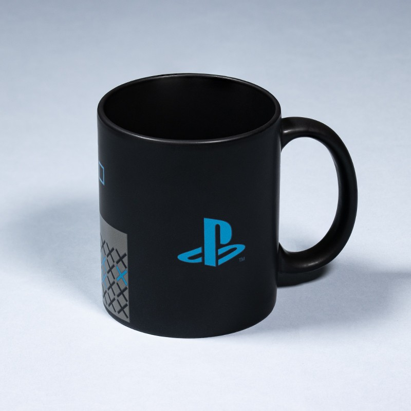 Una taza de cerámica negra con el logo azul de PlayStation en el lateral sobre fondo gris claro.