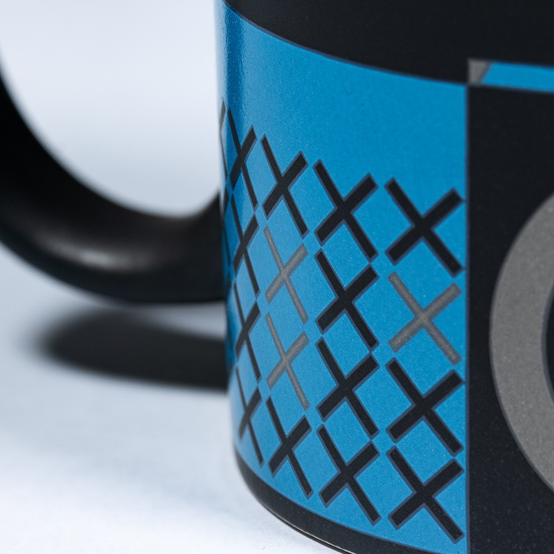 Una taza negra con un patrón azul de cruces y círculos grises.