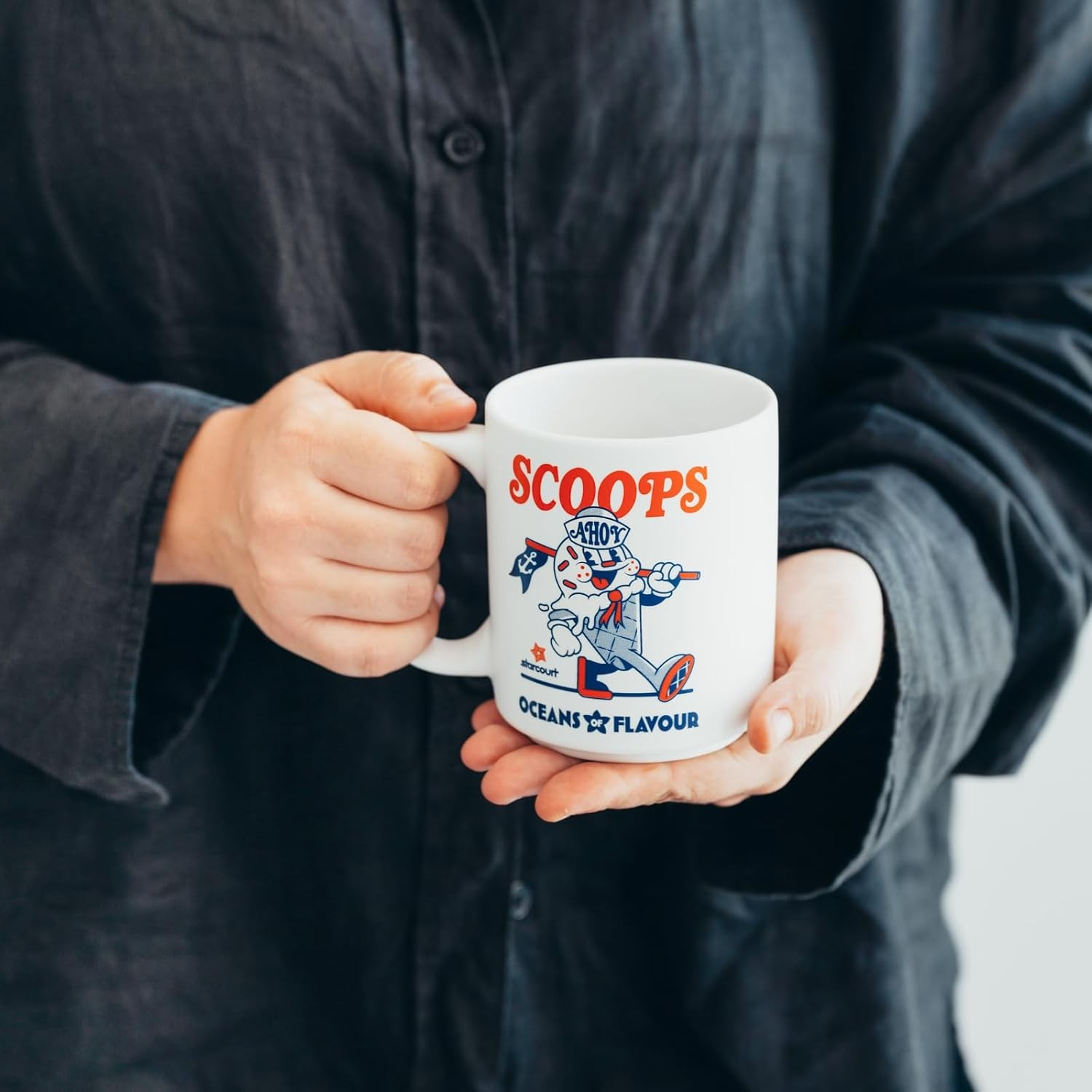 Una persona con una camisa oscura sostiene una taza blanca con un gráfico impreso.