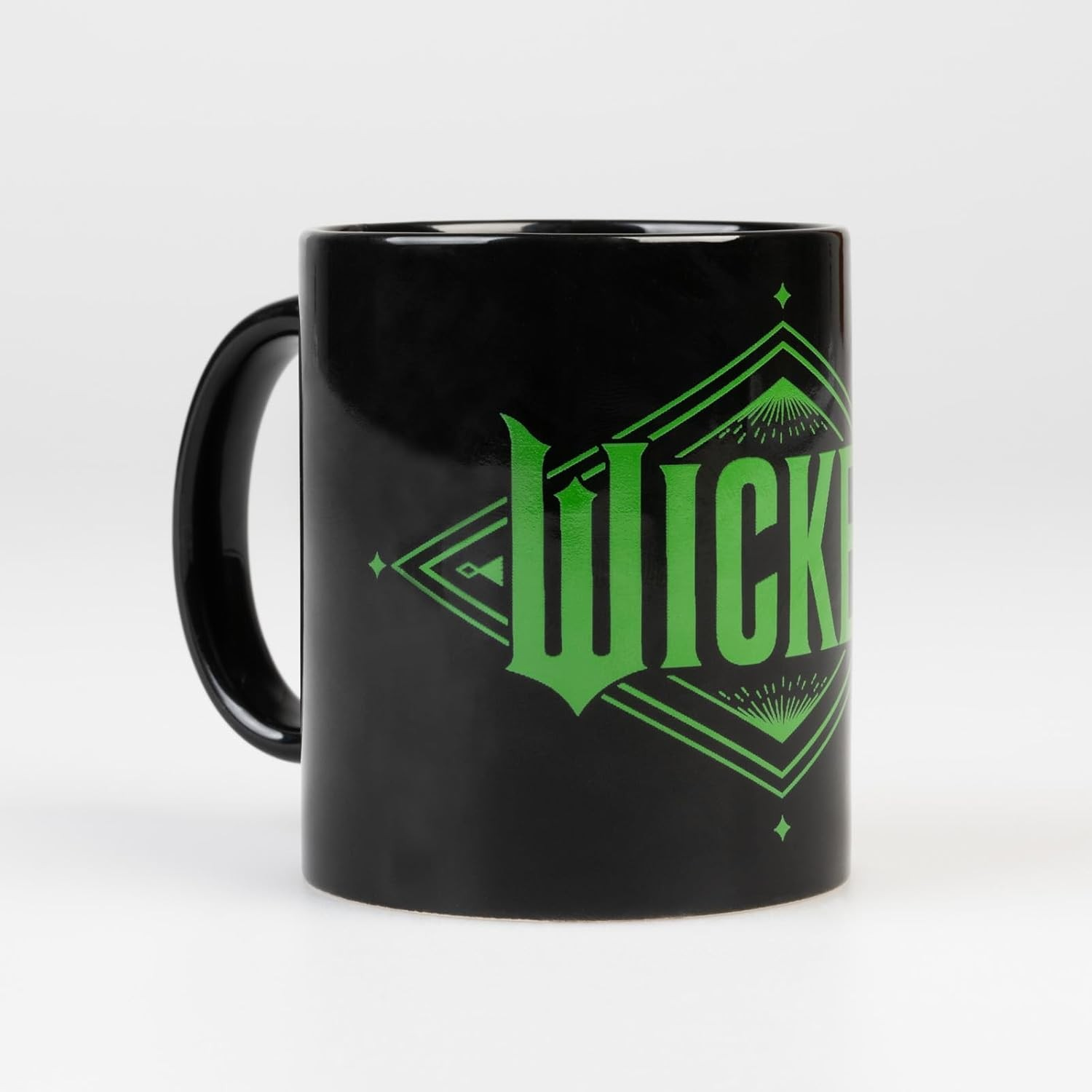 Una taza de cerámica negra tiene un logo verde de Wicked y diseños geométricos sobre fondo blanco.