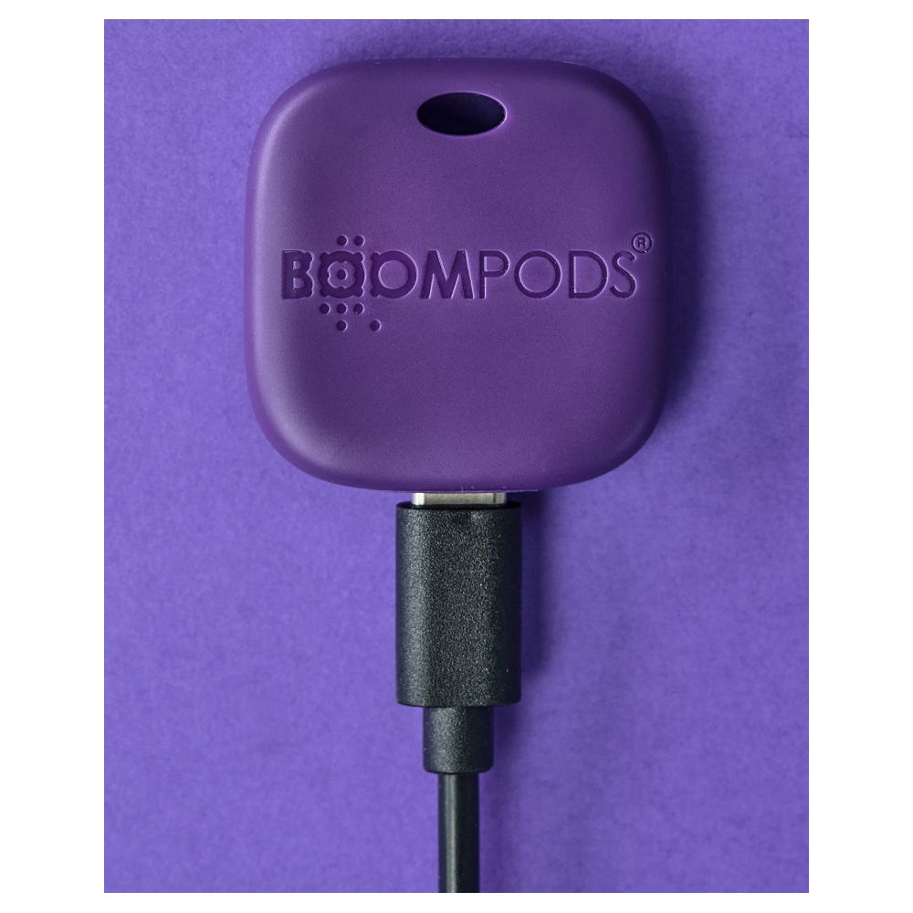 Ein lila Boompods-Gerät mit Bandloch ist an ein schwarzes USB-C-Kabel vor lila Hintergrund angeschlossen.