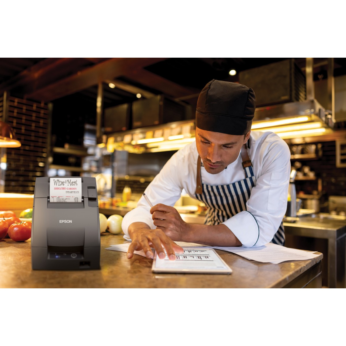 Chef in a restaurant works on a tablet, with an Epson receipt printer next to him.