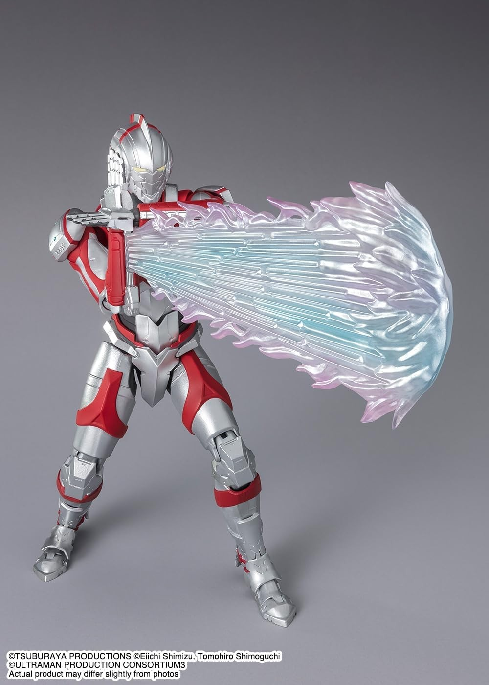 Una figura de acción de Ultraman roja y plateada dispara un rayo de energía azul y rosa contra un fondo gris.