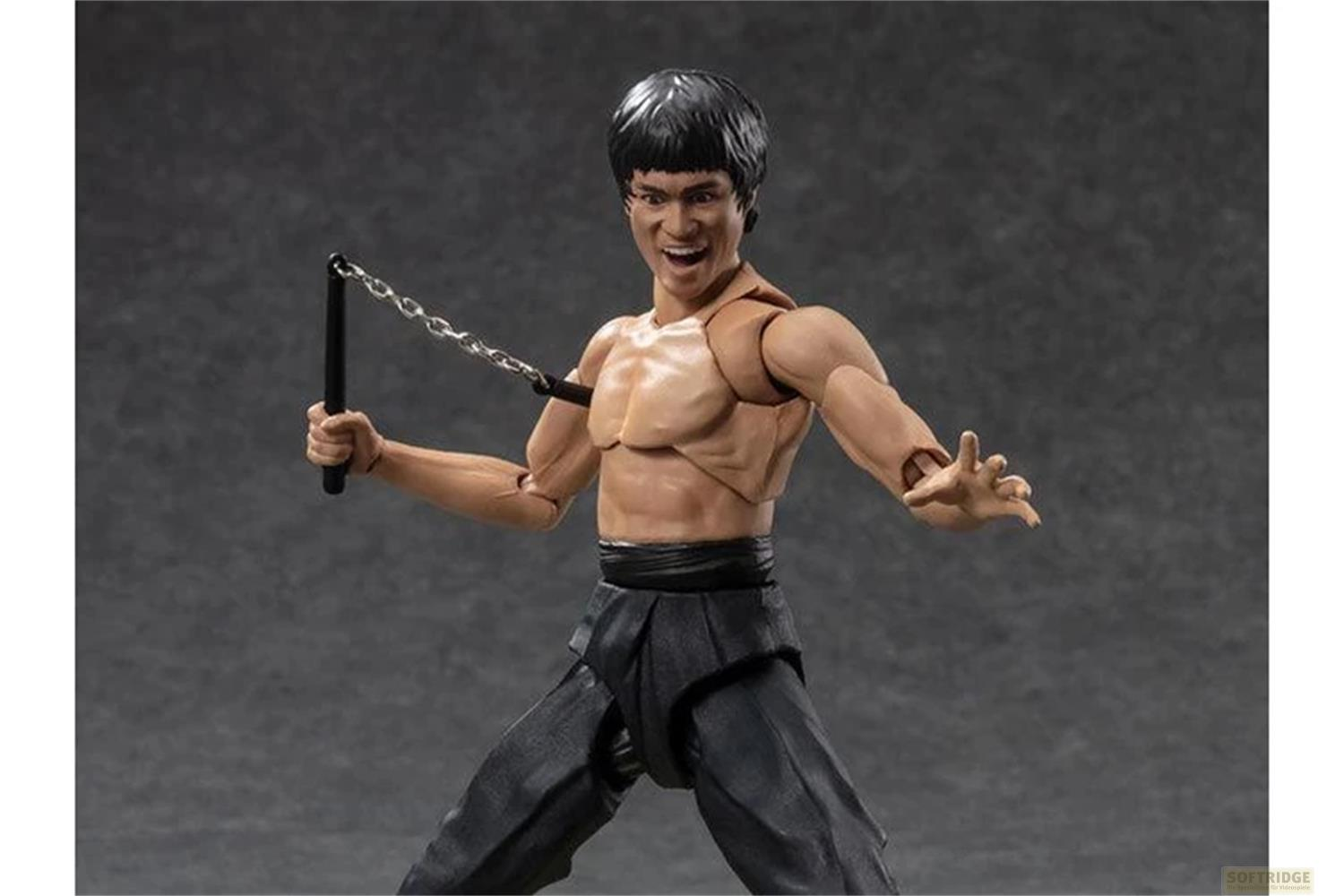 Figura de acción de Bruce Lee sosteniendo nunchakus, con pantalones negros y gritando, sobre fondo gris.