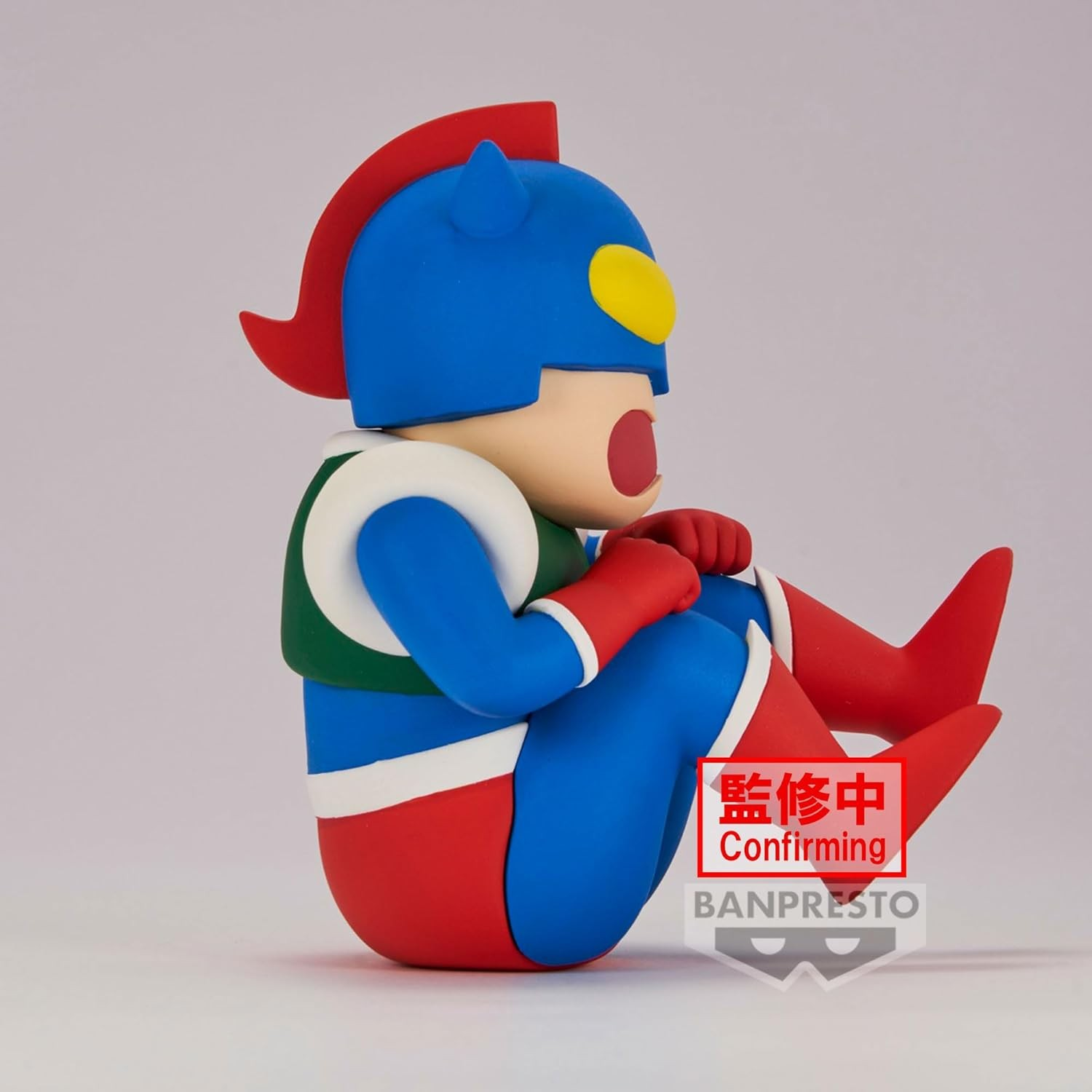 Una colorida figura de superhéroe sentada con casco azul, cresta roja y torso verde sobre fondo blanco.