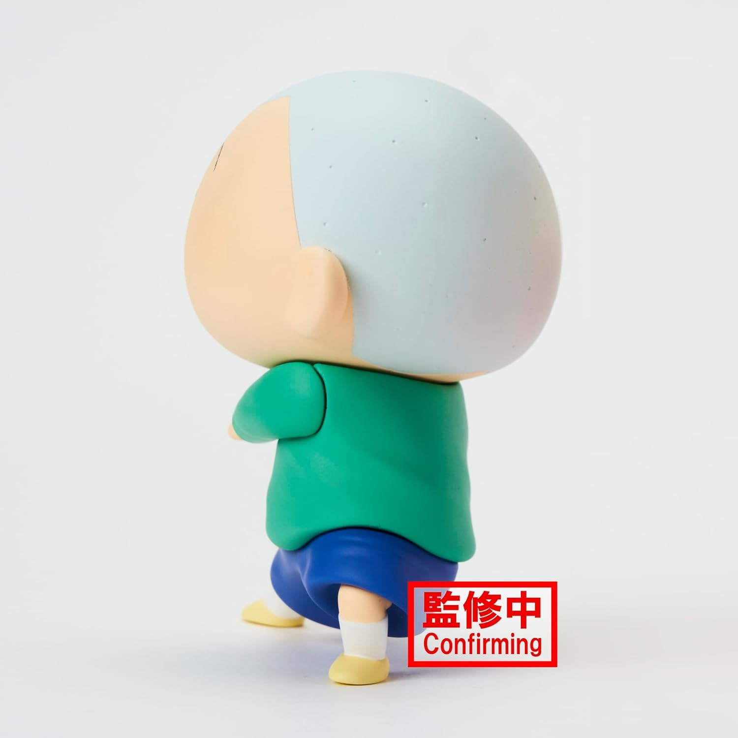 Una figura de anime calva con camisa verde, pantalones cortos azules y zapatos amarillos sobre fondo blanco.