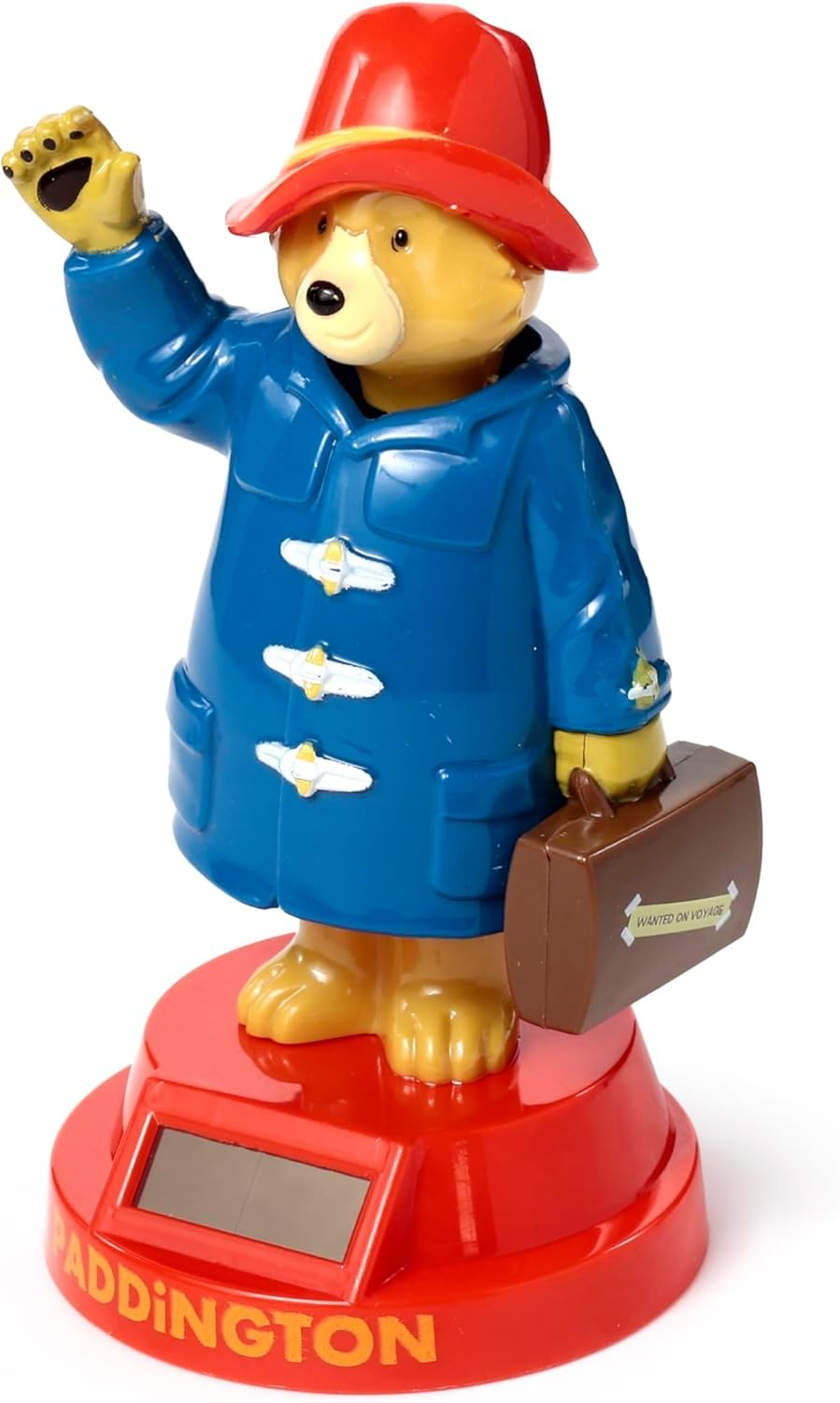 Una figura de Paddington Bear con abrigo azul, sombrero rojo y maleta, saludando sobre una base roja.
