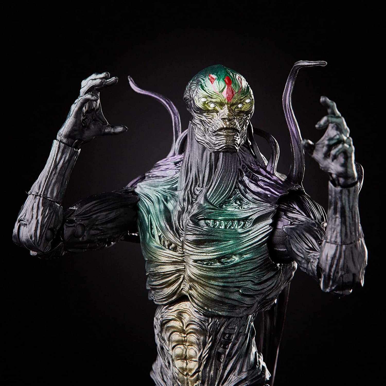 Detallada figura de acción alienígena con tentáculos, cuerpo metálico verde y manos levantadas sobre fondo negro.