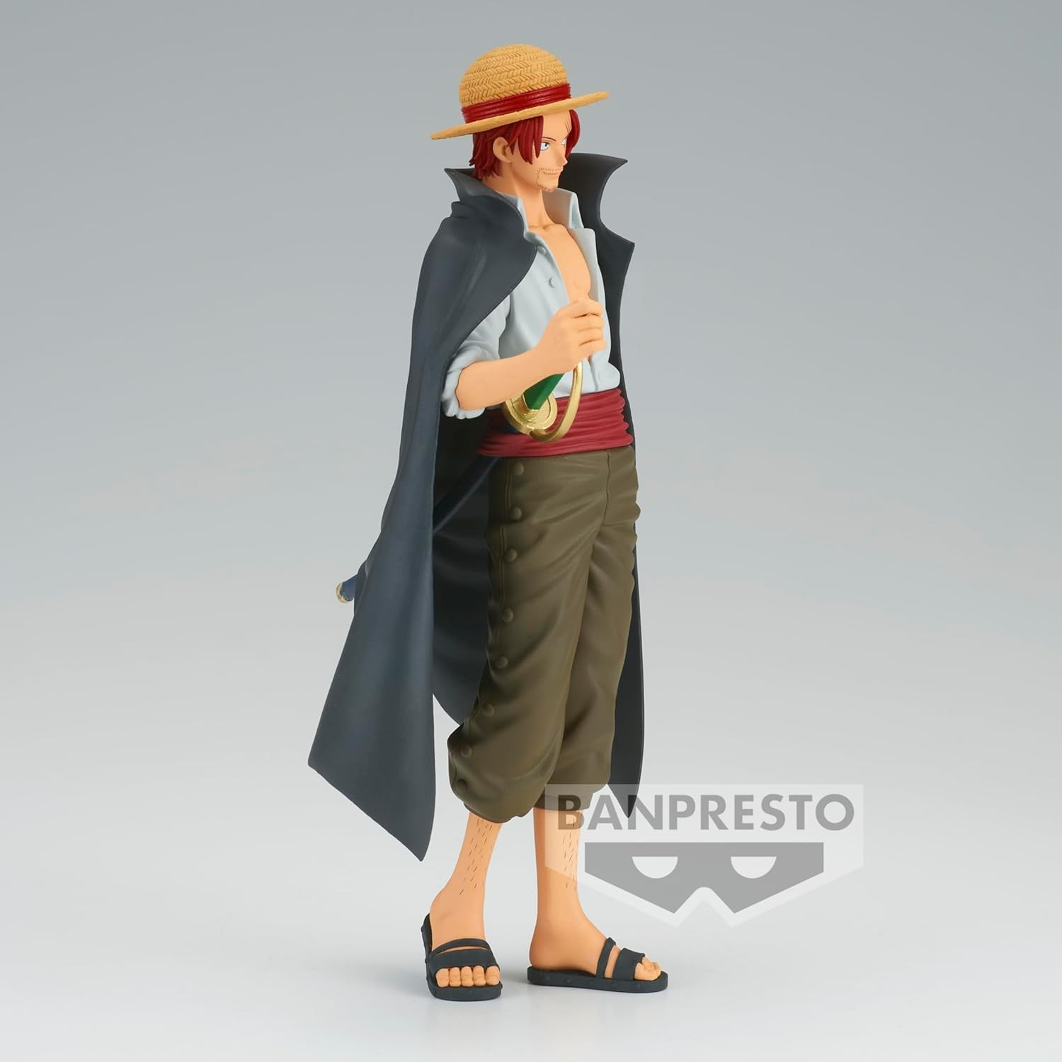 Una figura de Shanks de One Piece, con sombrero de paja, capa oscura y pantalones verdes sobre fondo claro.