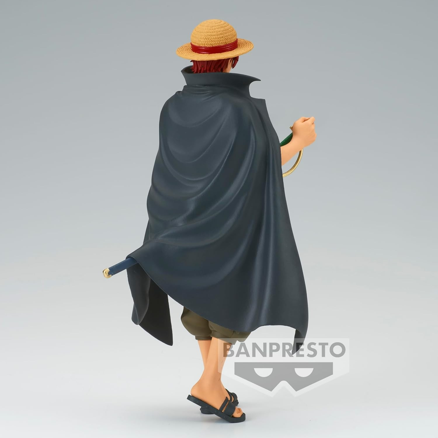 Vista trasera de una figura de Shanks con sombrero de paja, capa negra y espada sobre fondo gris.