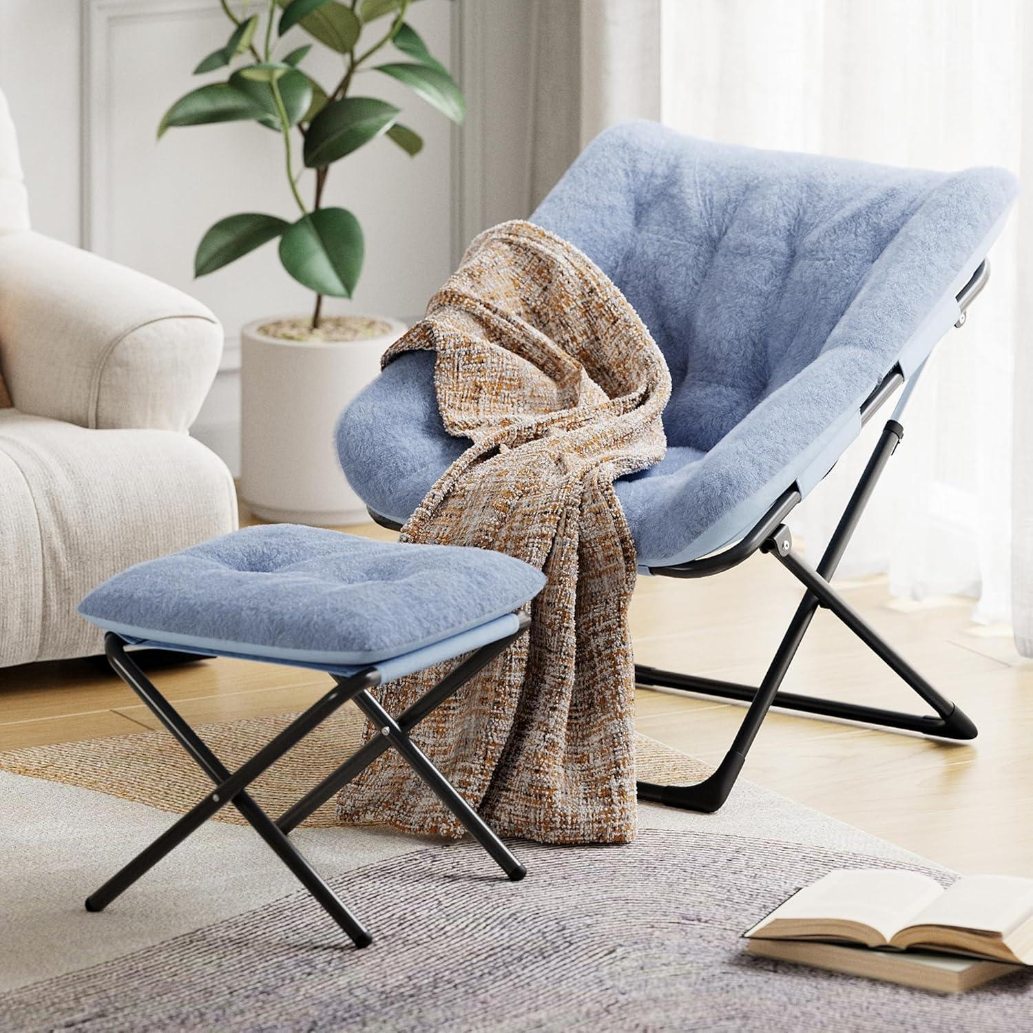 Poltrona pieghevole blu pelosa e pouf con coperta, vicino a una pianta e libri.