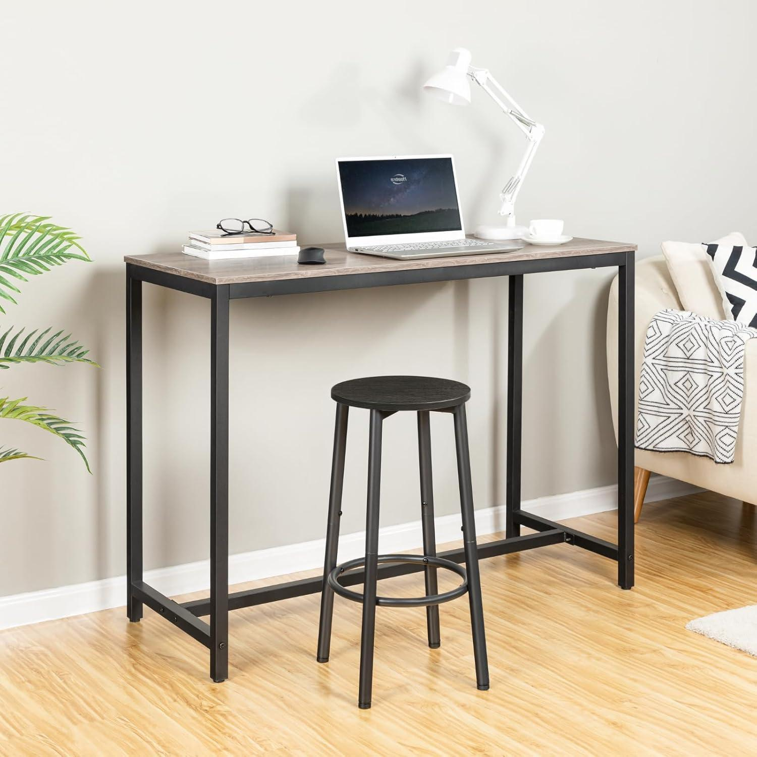 Scrivania in legno con struttura in metallo nero, laptop, lampada e uno sgabello nero coordinato.