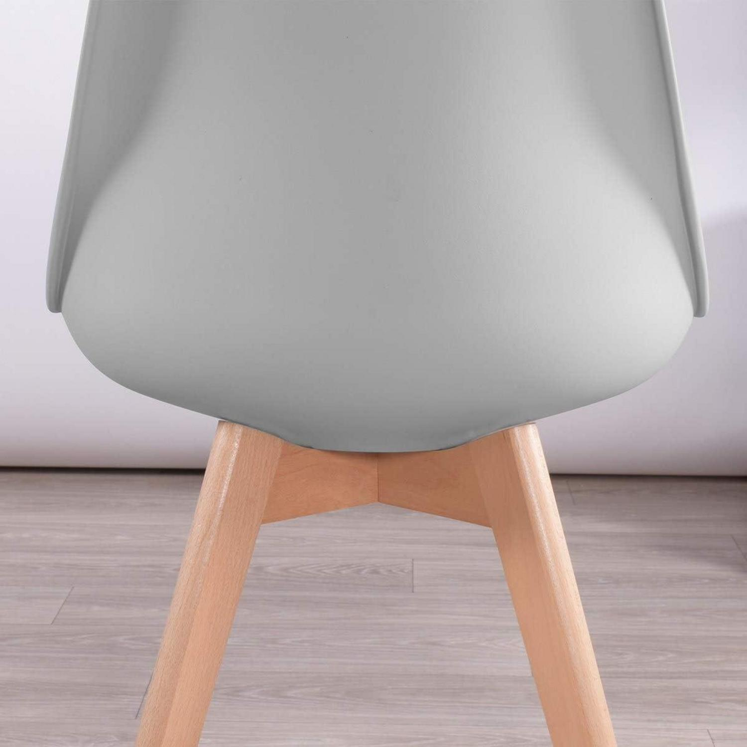 Parte inferiore di una sedia grigia con quattro gambe in legno su sfondo chiaro.