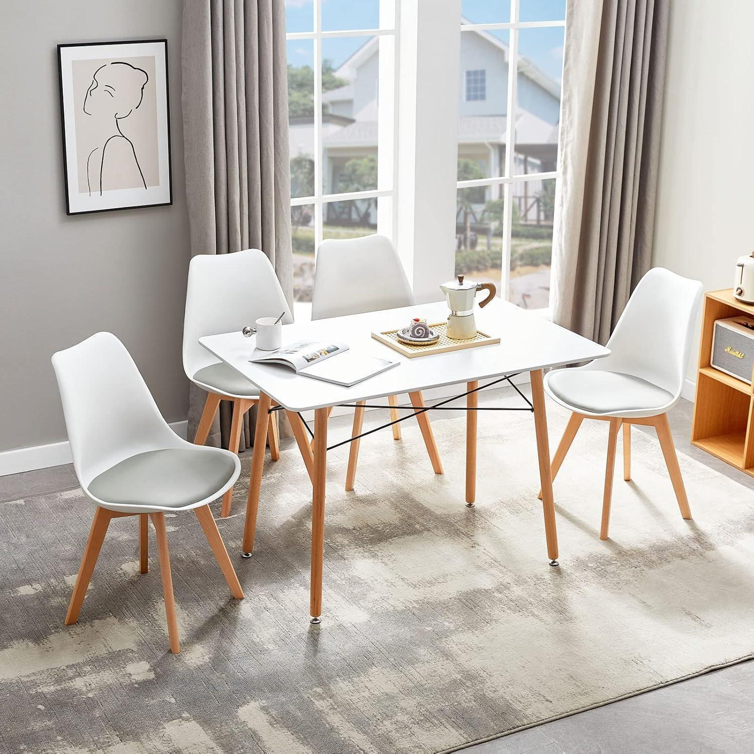 Un tavolo da pranzo bianco con quattro sedie e gambe in legno si trova su un tappeto in una stanza luminosa.