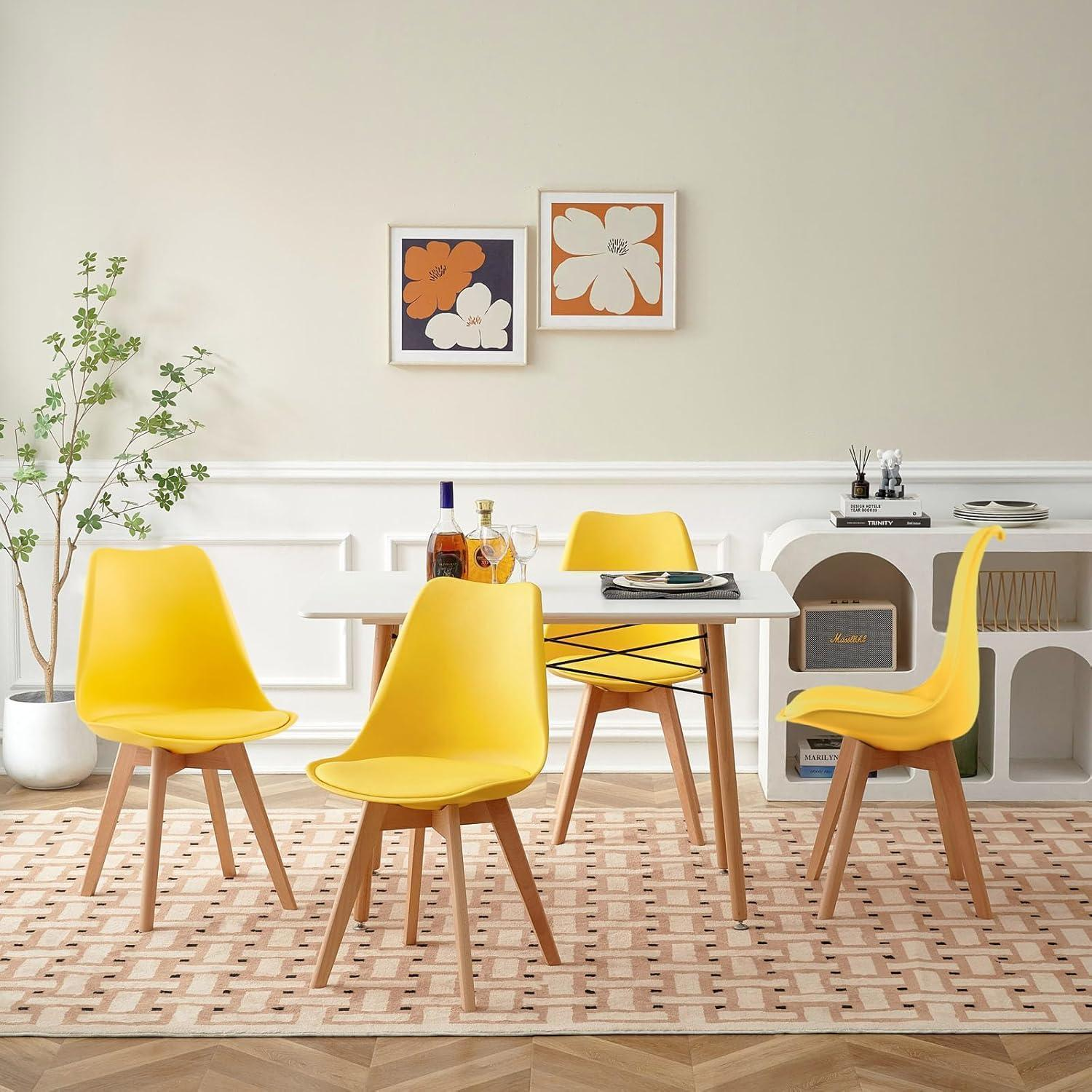 Sala da pranzo con quattro sedie gialle, tavolo bianco, arte da parete astratta e pianta.