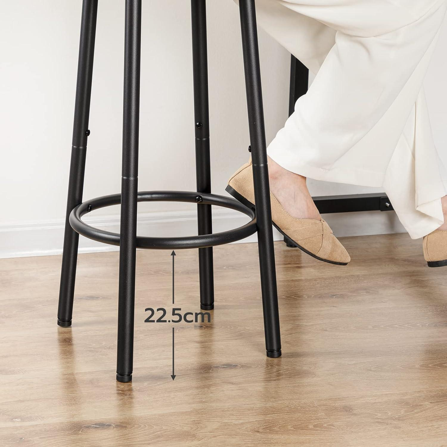 Persona seduta su sgabello nero con poggiapiedi su pavimento in legno, altezza 22,5cm.