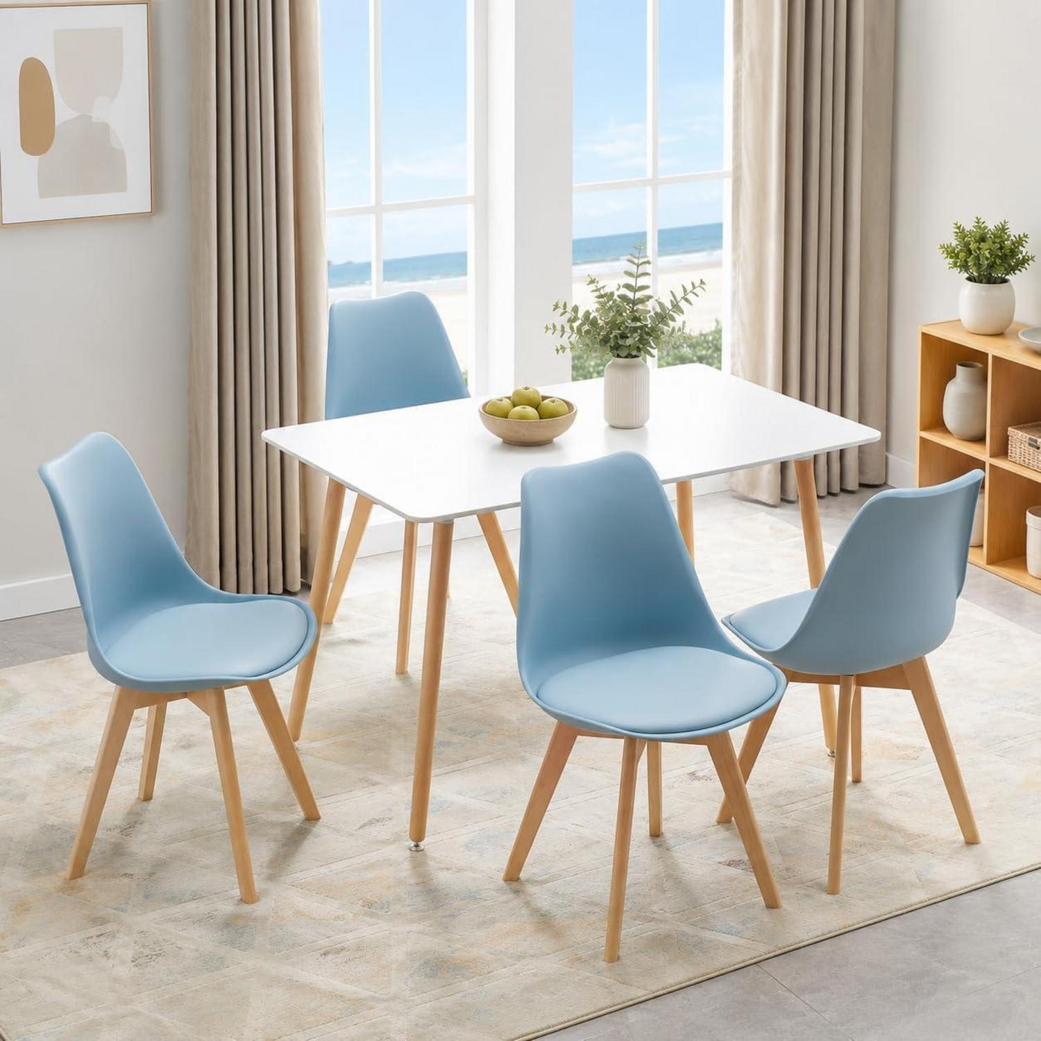 Un tavolo da pranzo bianco con quattro sedie azzurre e gambe di legno si trova davanti a una finestra con vista mare.