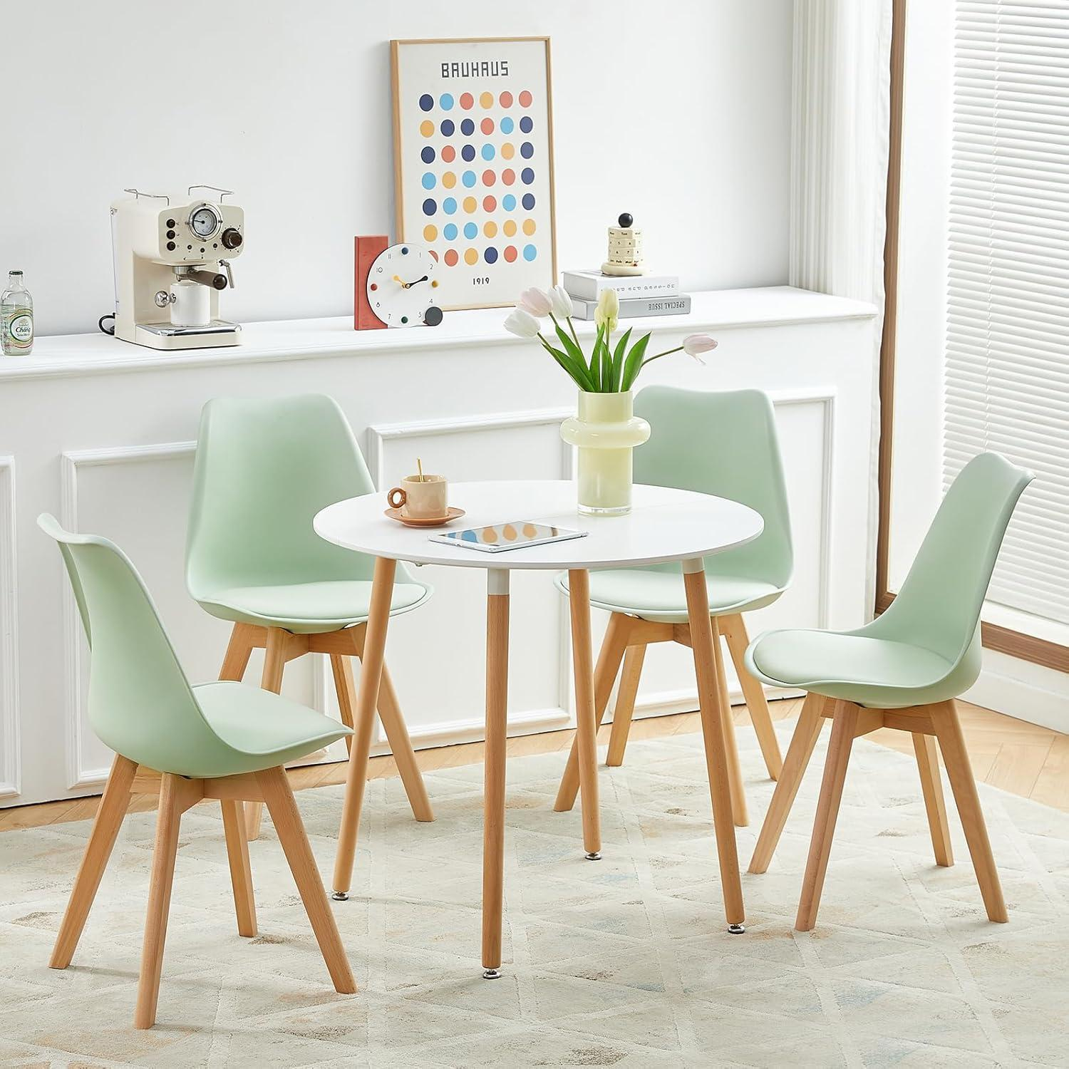 Un tavolo da pranzo rotondo bianco con quattro sedie verde pastello su un tappeto in una stanza luminosa.