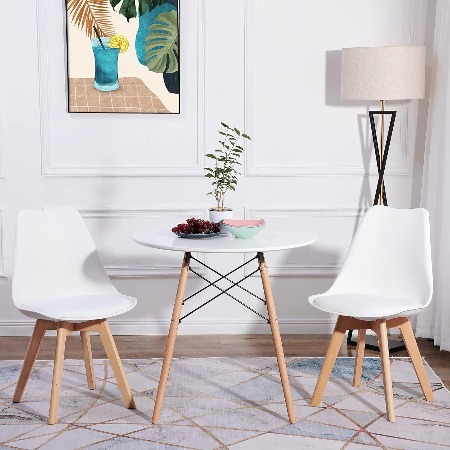 Un tavolo rotondo bianco con due sedie, frutta, una pianta, una lampada e un quadro.