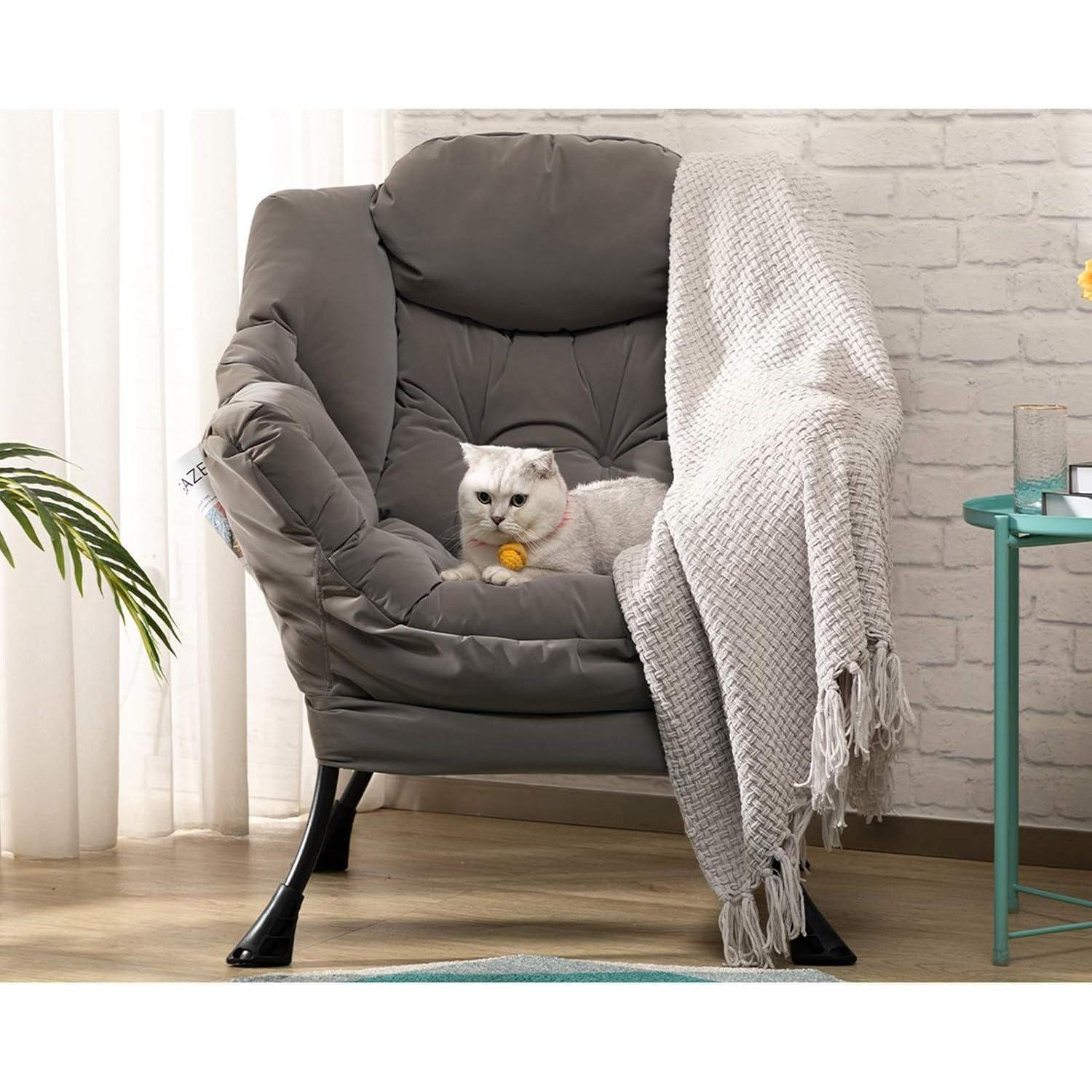 Un gatto bianco siede su una comoda poltrona grigia con una coperta e un piccolo tavolo.