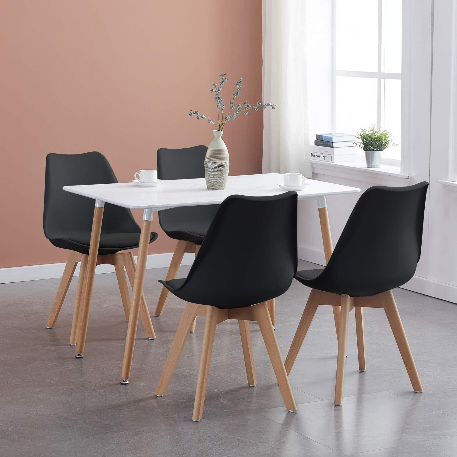 Un tavolo bianco con quattro sedie nere e gambe in legno in una stanza con pareti beige e finestra.