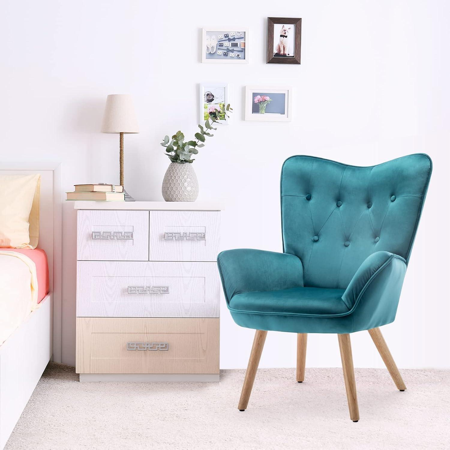 Una poltrona trapuntata verde acqua con gambe in legno accanto a una cassettiera bianca con lampada e foto.