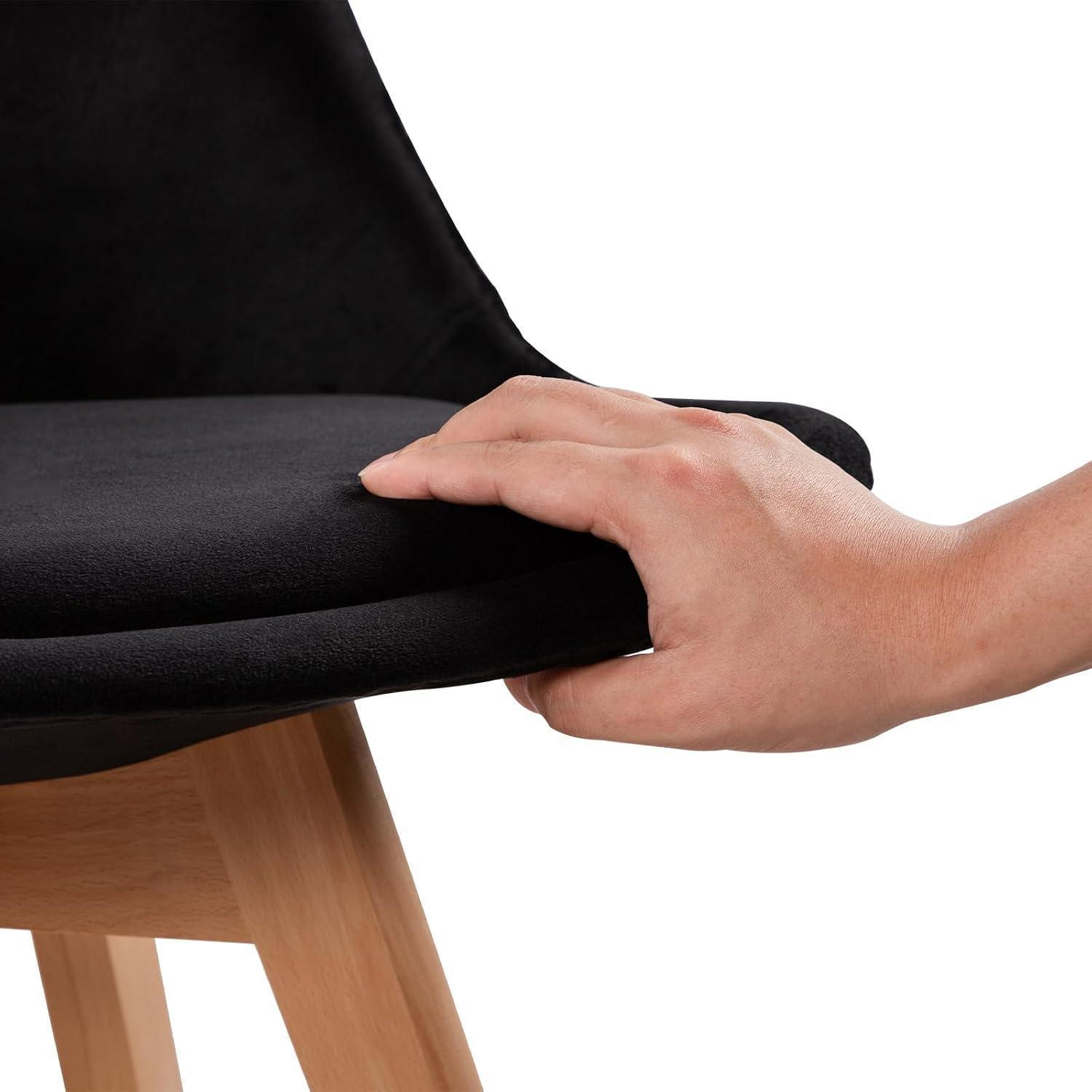 Una mano tocca il sedile in velluto nero di una sedia con gambe in legno su sfondo bianco.