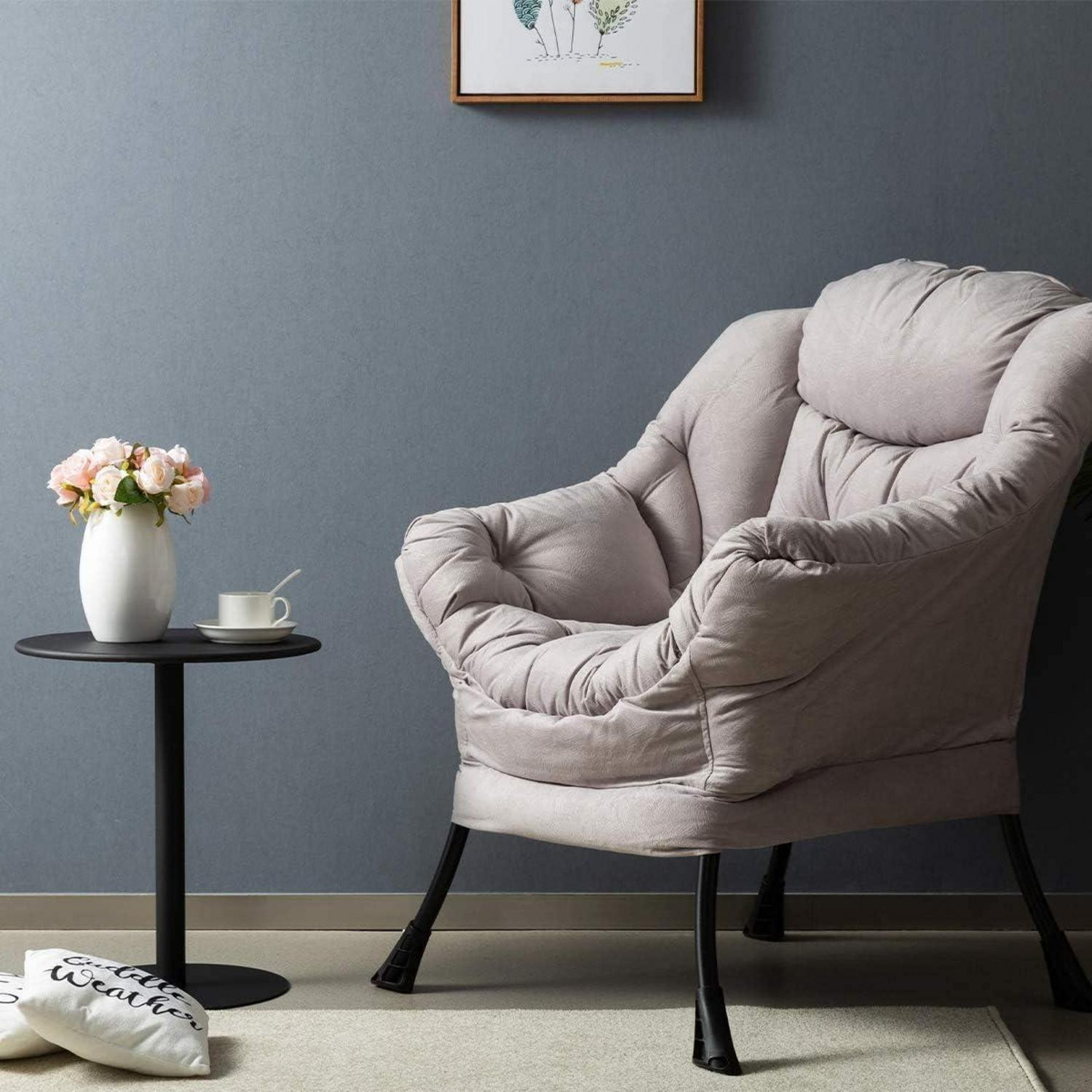 Una poltrona grigia con gambe nere è accanto a un piccolo tavolo con un vaso di fiori e una tazza.