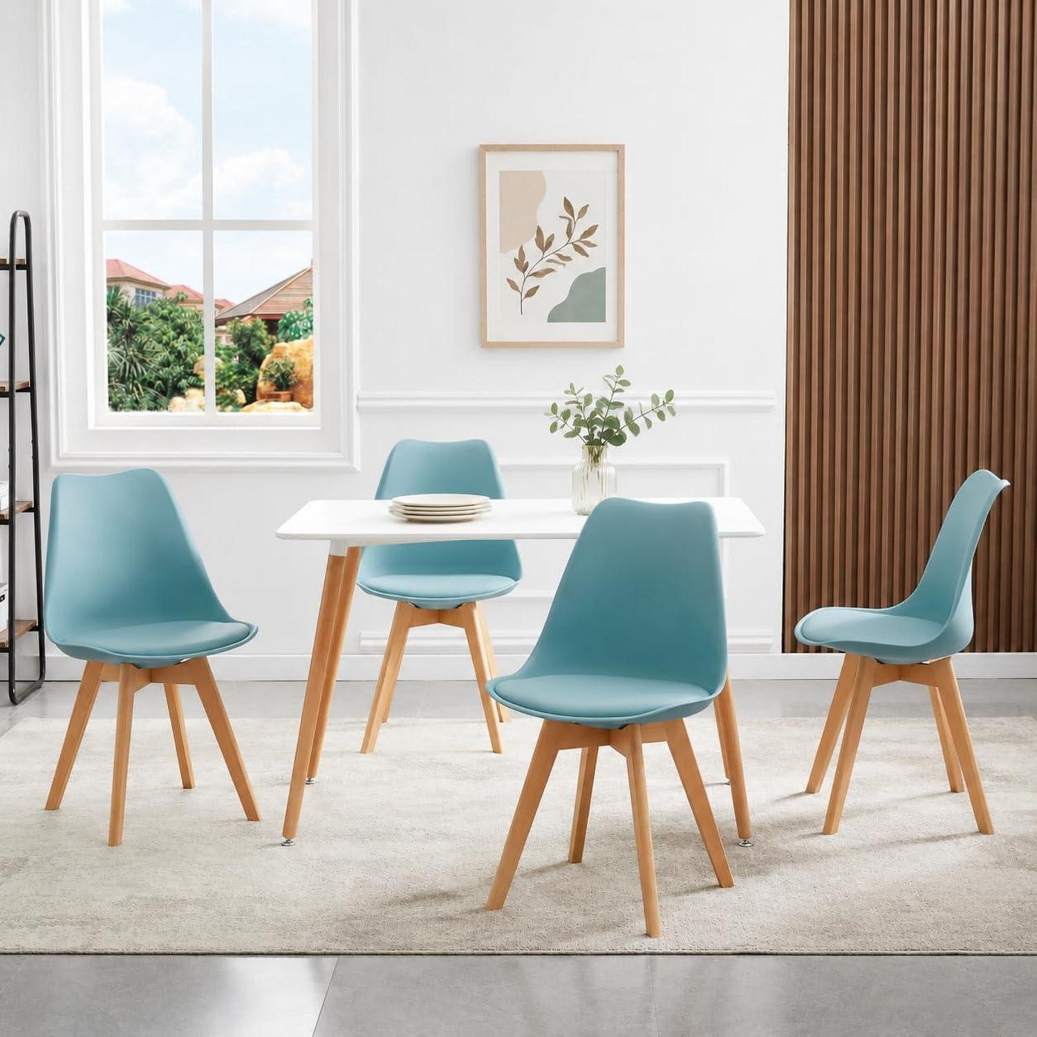 Un tavolo da pranzo bianco con quattro sedie azzurre e gambe in legno si trova su un tappeto in una stanza luminosa.